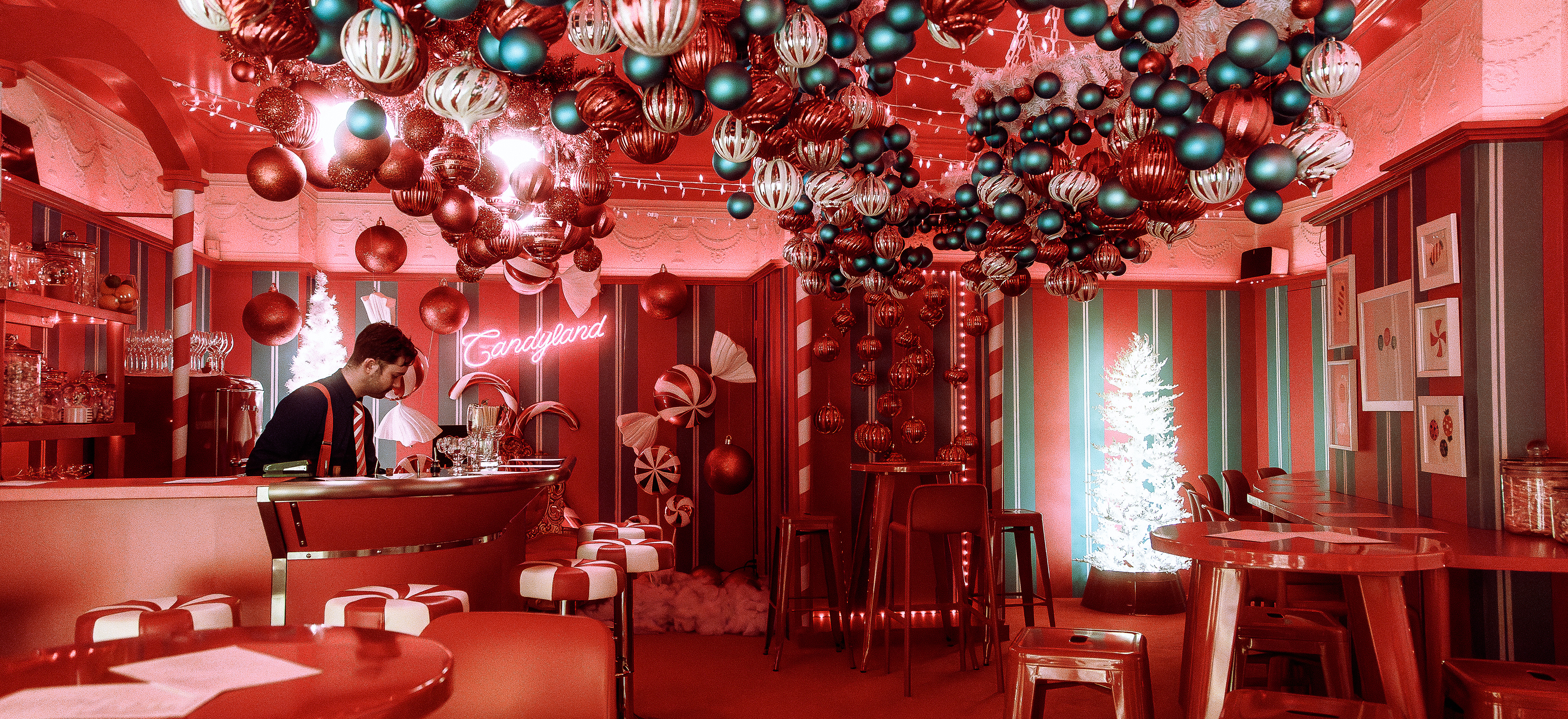Plan large du Elf Pub, un pub éphémère décoré pour le temps des fêtes. Les murs et le tapis est rouge, il y a des boules de noël accroché au plafond.