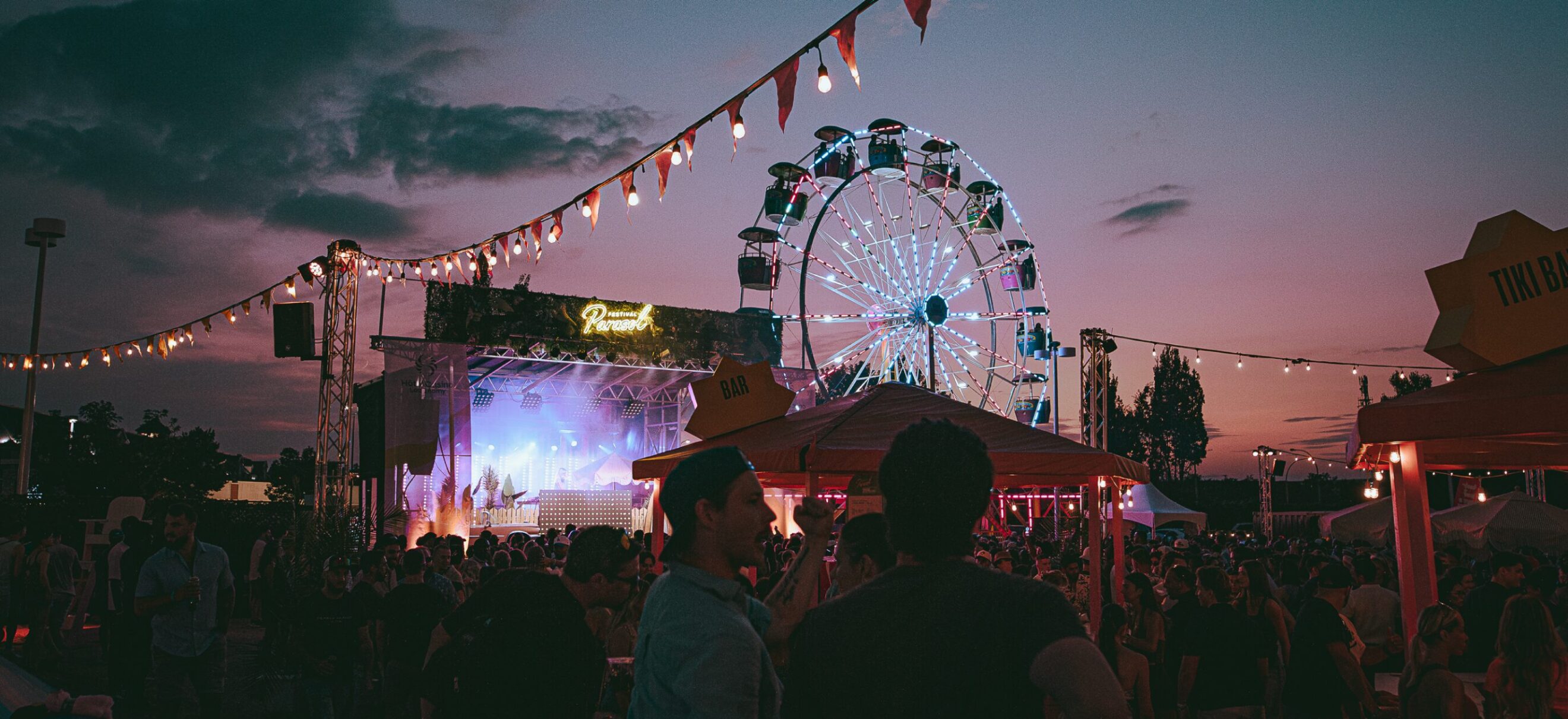 Foule devant la scène du festival parasol ainsi que la grande roue au couché du soleil.